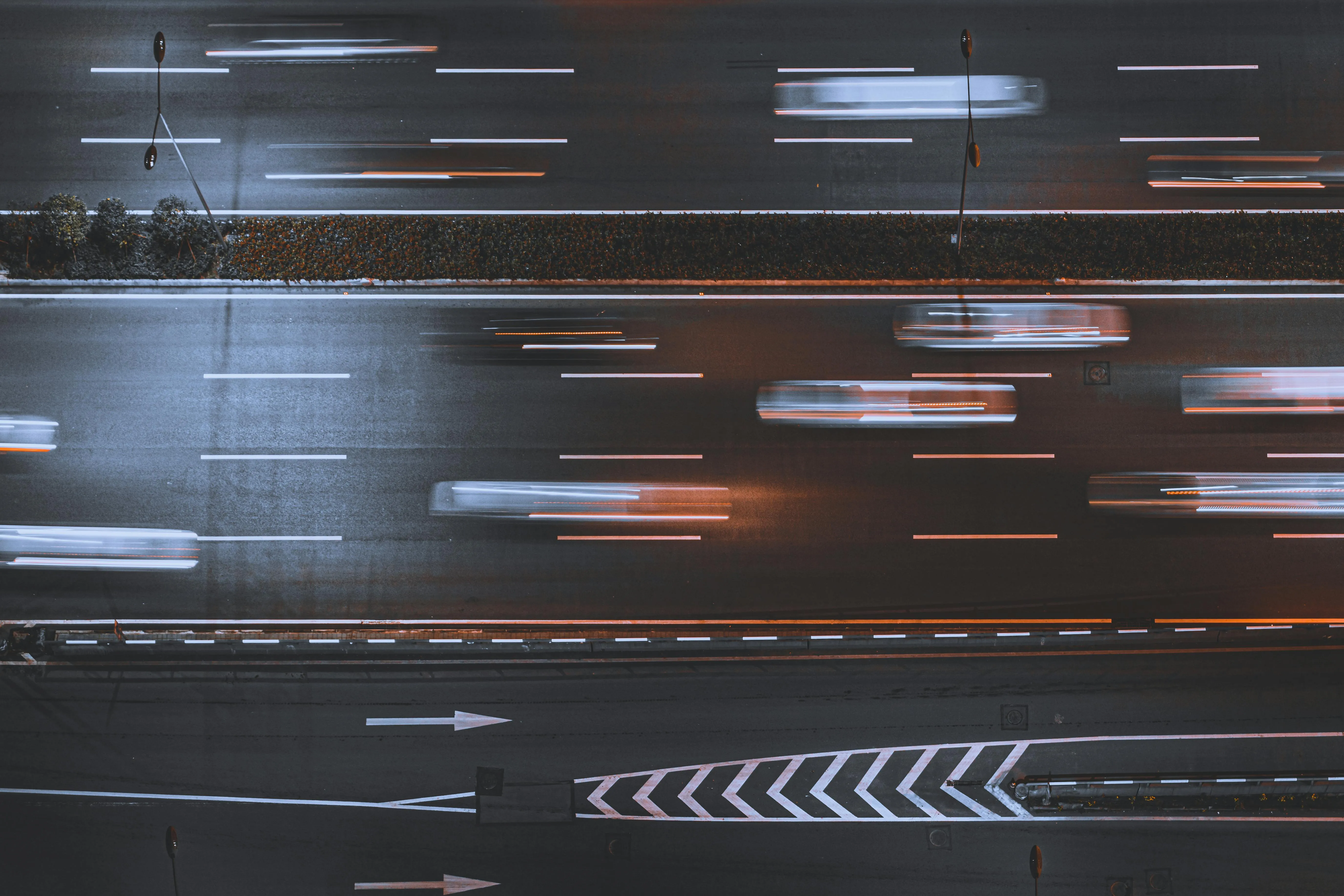 Top down view of a multi-lane road at night with cars travelling across with a trail of lights following the cars.